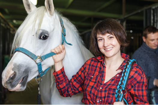 Woman smiling with white horse in barn.